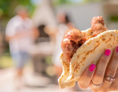 Mano con un panino e salsicce, sfondo sfocato di persone.