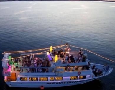 Partyboot bei Sonnenuntergang mit bunten Lichtern und Menschen an Bord.