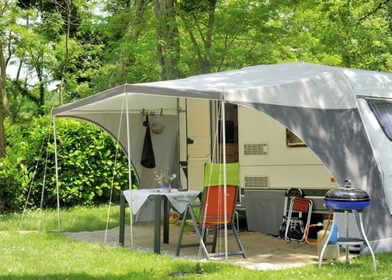 Campeggio con roulotte, tavolo, sedie e barbecue in una zona verde.