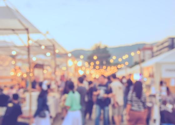 Mercato all'aperto con luci e persone sfocate.