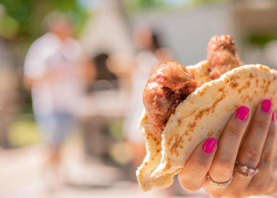 Mano con un panino e salsicce, sfondo sfocato di persone.