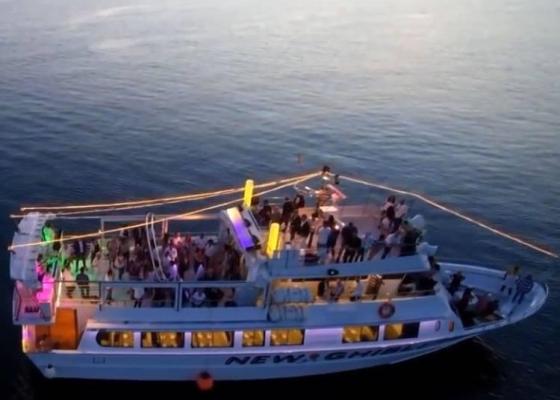 Partyboot bei Sonnenuntergang mit bunten Lichtern und Menschen an Bord.