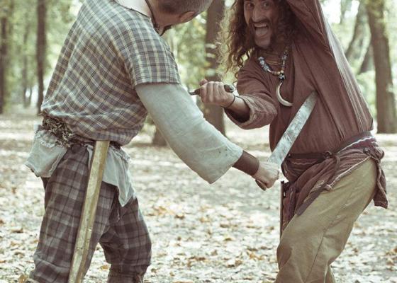 Due uomini in abiti antichi combattono con spade nel bosco.